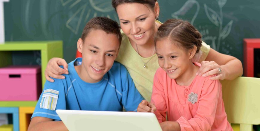 Portrait of happy mother and children sitting at table with laptop